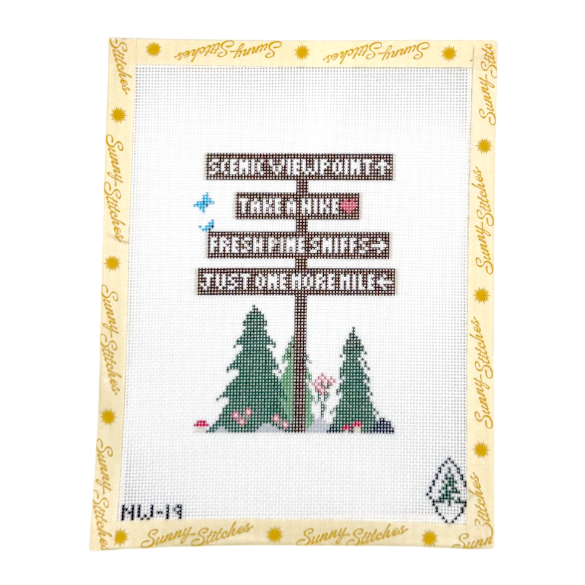 A framed needlepoint canvas featuring a wooden signpost with directional signs reading 'SCENIC VIEWPOINTS', 'TAKE A Hike', 'FRESH PINE SNIFFS', and 'JUST ONE MORE MILE', above two green pine trees with small pink flowers. The canvas is bordered by a cream frame printed with the brand name 'Sunny Stitches'.