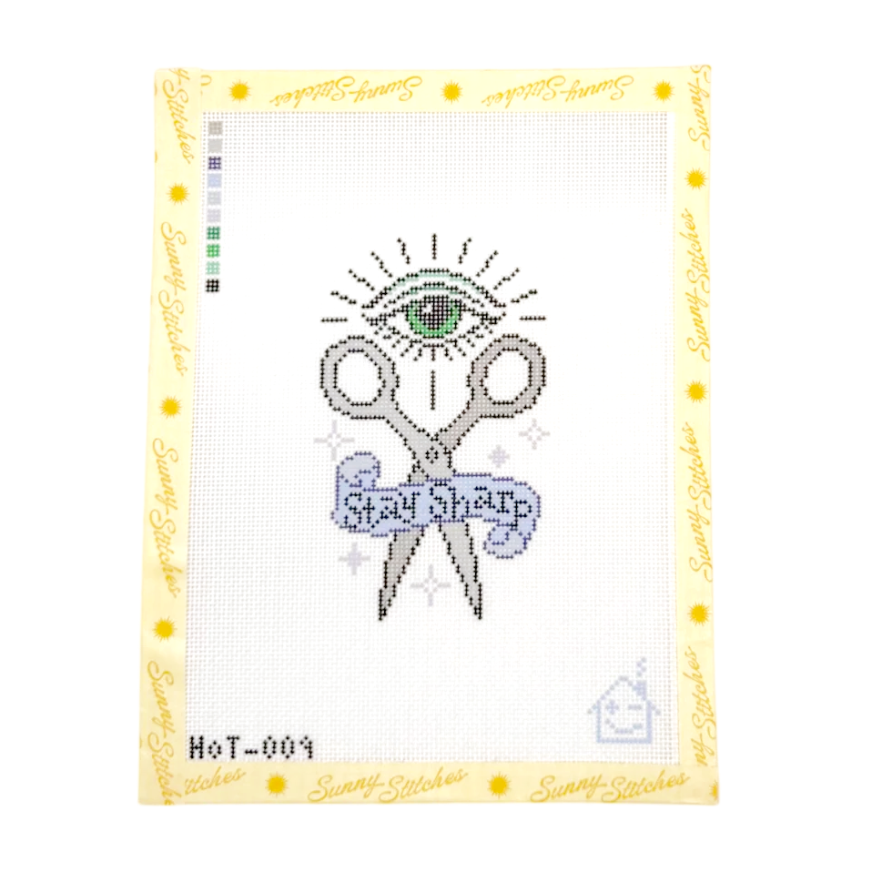 A cross-stitch pattern from Sunny Stitches featuring a needlepoint-style design of scissors with a green eye above them and a blue banner reading 'Stay Sharp'. The card has a white stitched grid area, a yellow border with 'Sunny Stitches' text, and a small color chart on the left.