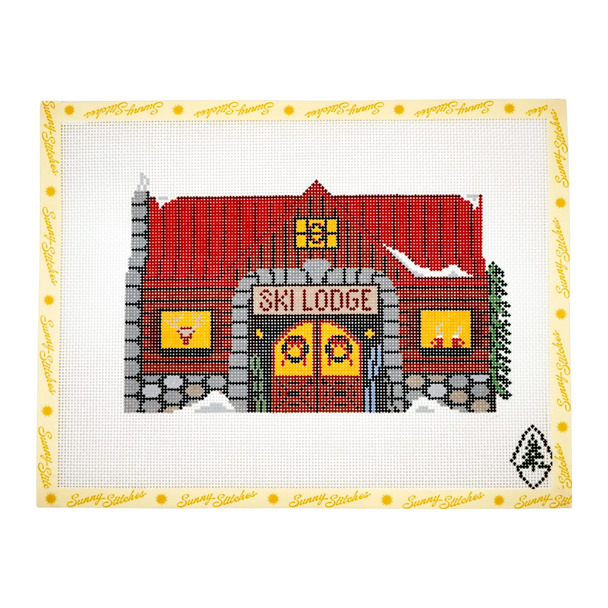 A completed cross-stitch needlework design of a rustic ski lodge with a red roof, gray stone walls, and yellow accents, displayed on a white Aida cloth with a yellow embroidered border.